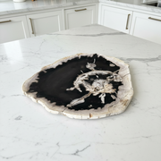 A round petrified wood slab clock face with a black center and white crystalline details, resting on a light gray tiled floor.