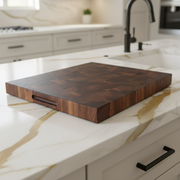 A rectangular dark wood cutting board with a built-in handle on one side, shown at an angle against a plain white background.