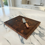 Wooden cutting board with a knife on a marble countertop in a kitchen.