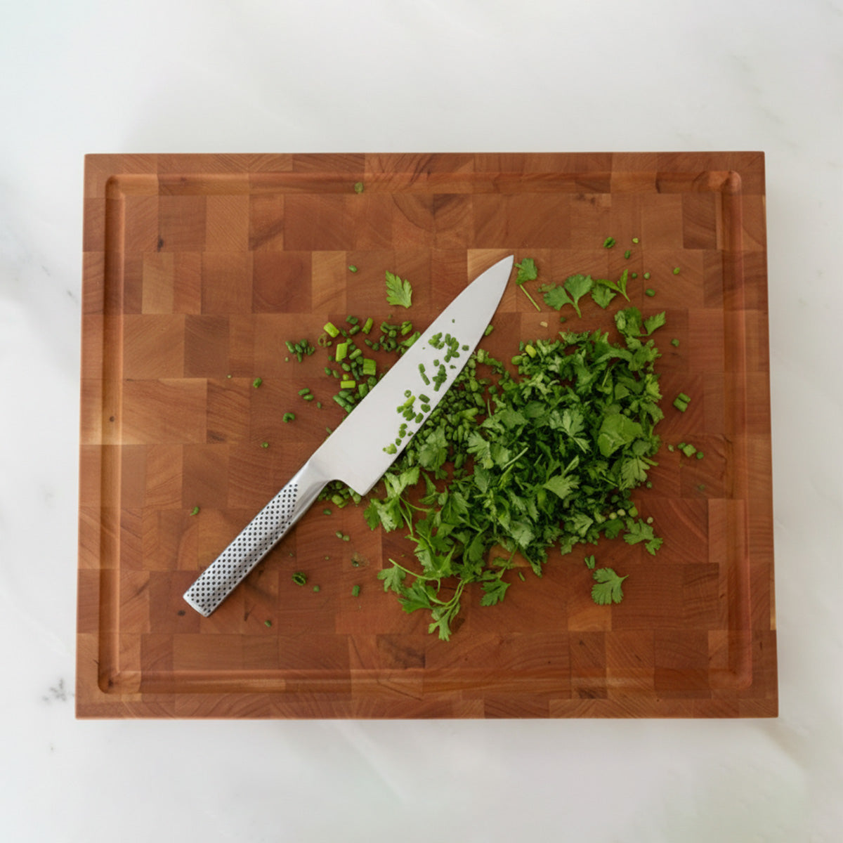 Wooden cutting board with chopped greens and a knife on a white background